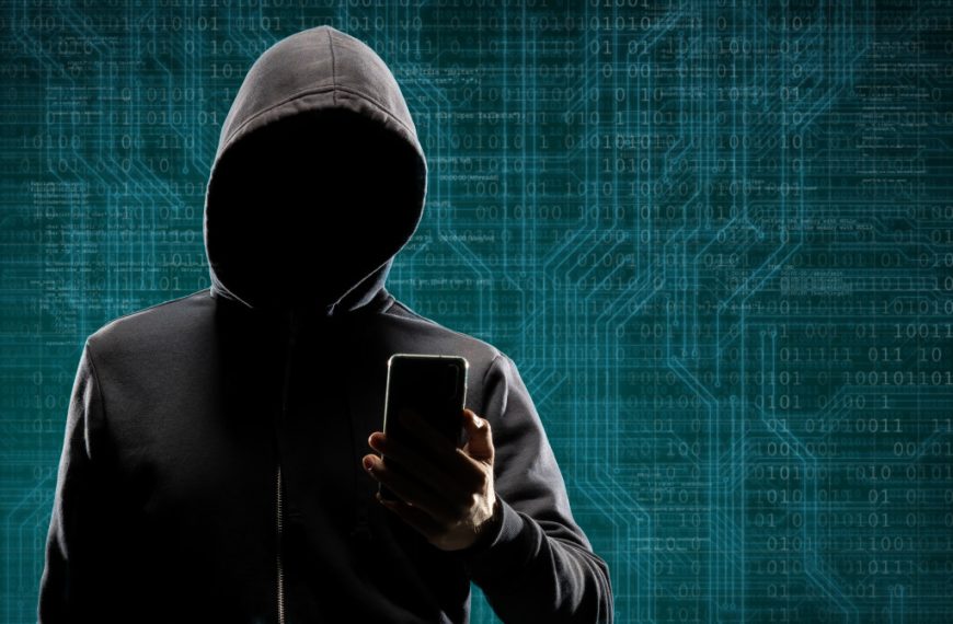 Computer hacker in mask and hoodie over abstract binary background