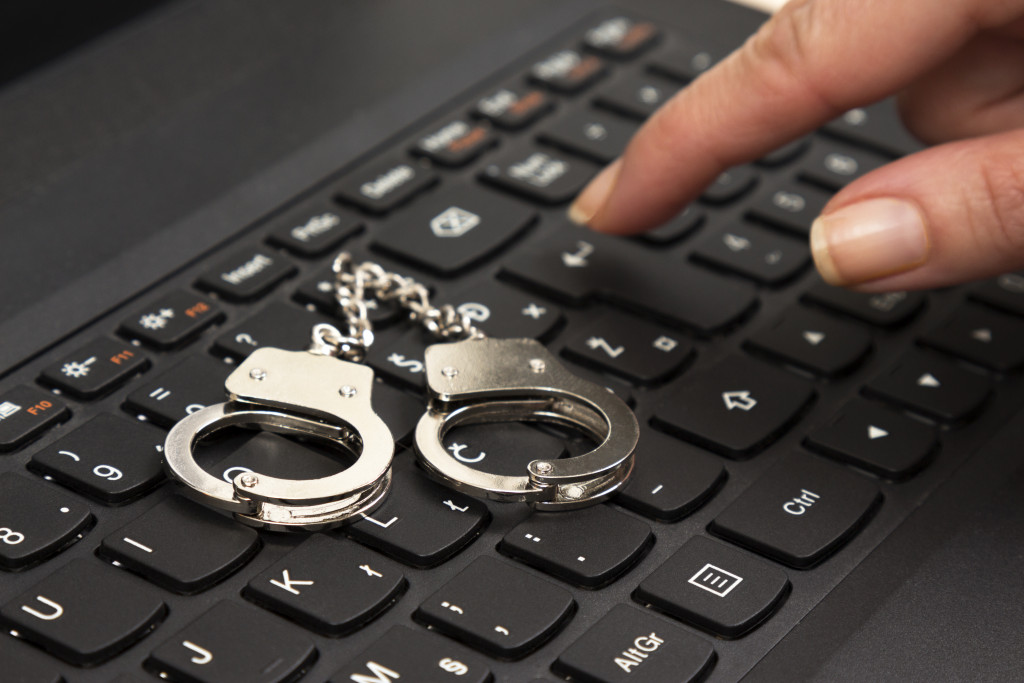Cybercrime concept with small handcuffs on computer keyboard and female hand pressing the enter key